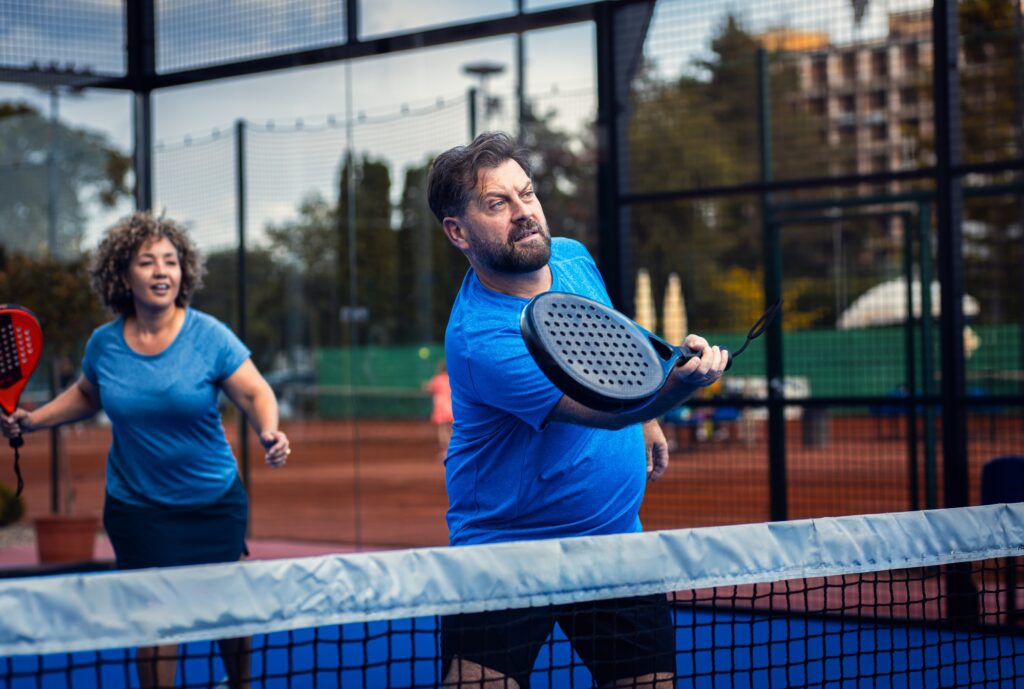 Mixed adult couple palying padel on outdoor court.